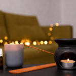 Black aroma lamp,candle flame and incense sticks against cozy warm lights on the home sofa.Empty space