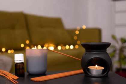 Black aroma lamp,candle flame and incense sticks against cozy warm lights on the home sofa.Empty space